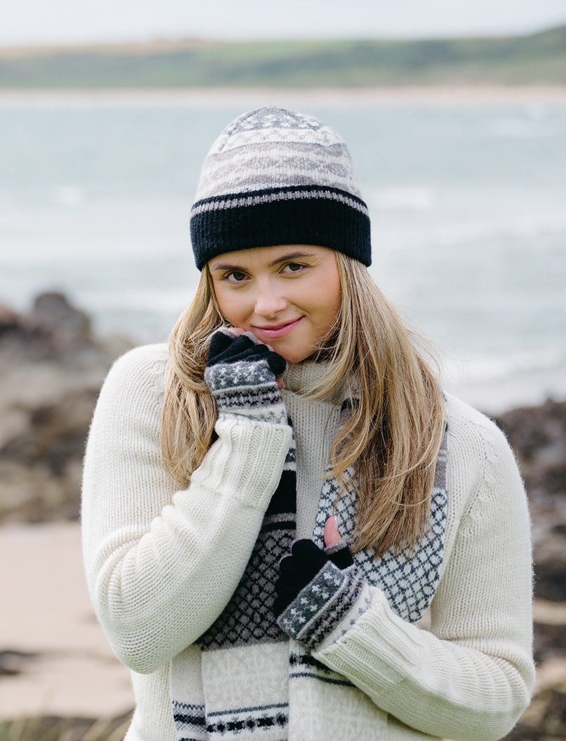 Girl wearing a neutral fair isle beanie hat with black ribbed turn back and matching fingerless gloves