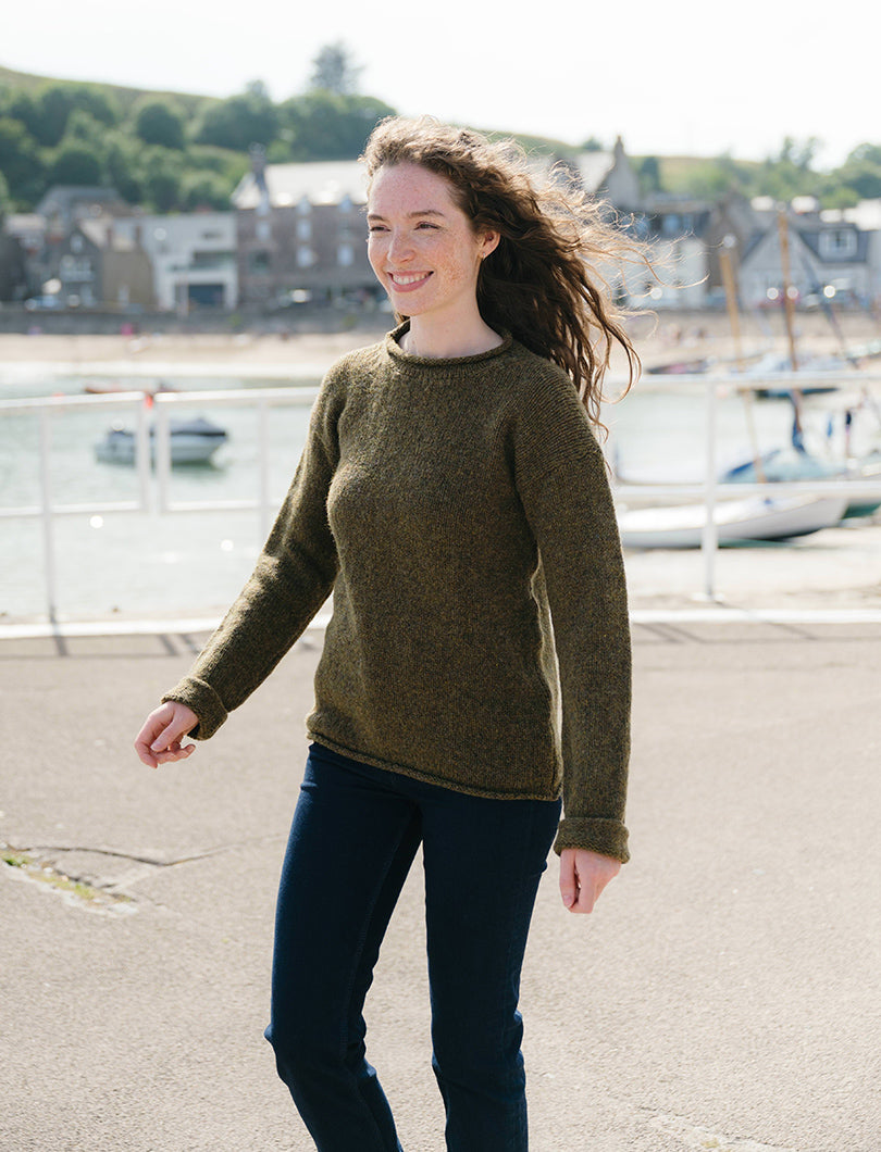 Woman wearing a green wool sweater standing outdoors with a harbour in the background