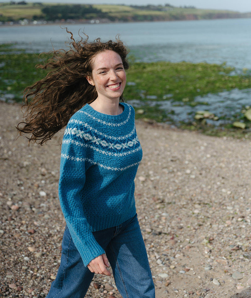 Womens walking on a beach wearing a turquoise textured fair isle jumper