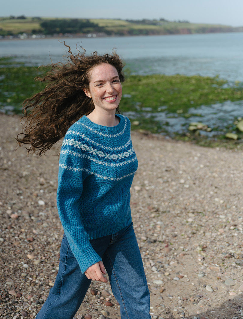 Womens walking on a beach wearing a turquoise textured fair isle jumper