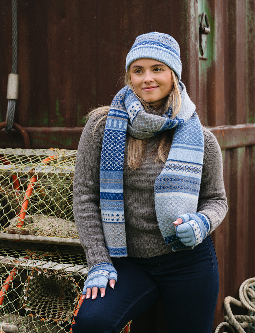 Girl wearing a fair isle scarf in tones of blue with matching fingerless gloves and hat
