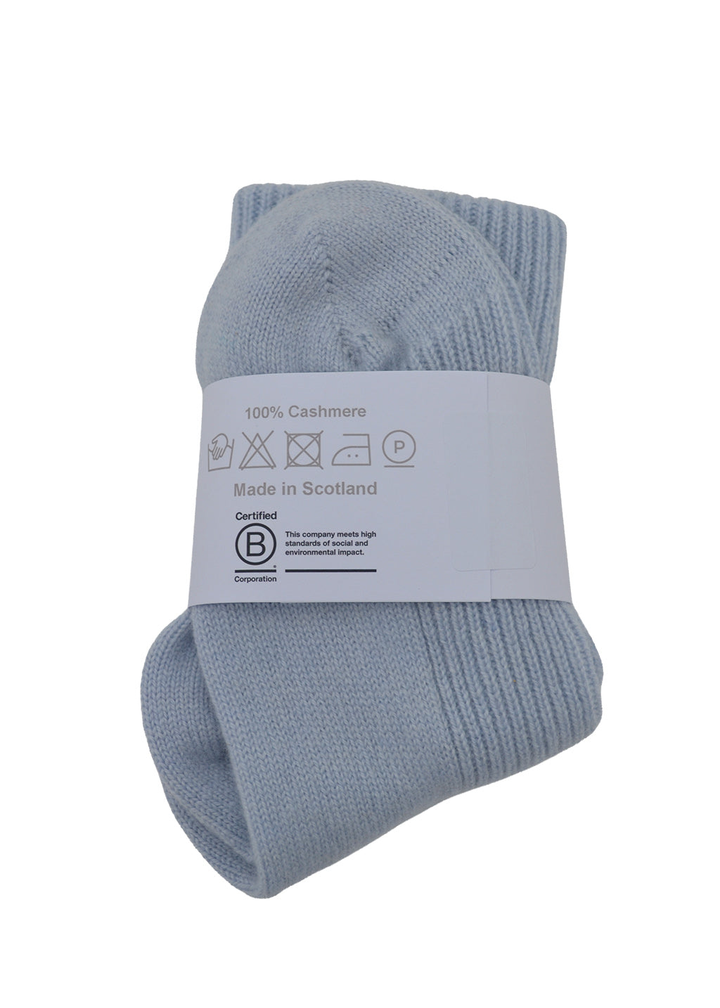 A pair of light blue ribbed knit socks bundled together with a white paper label that reads '100% Cashmere Made in Scotland' and shows care instructions and a B Corp certification logo.