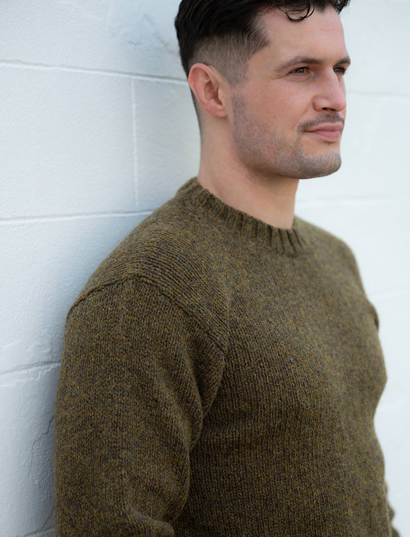 Man wearing a moss olive green sweater against a white wall