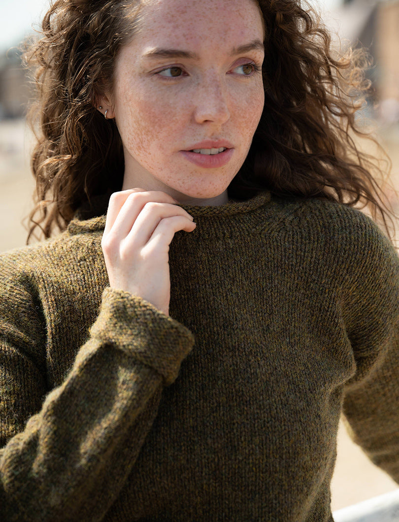 women wearing an olive green jumper with turned back cuffs, holding the rolled neck