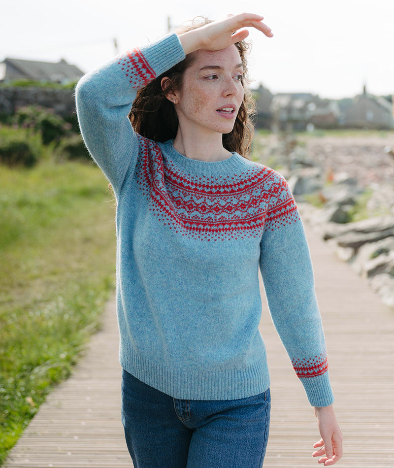 Woman wearing a duck egg blue sweater with red fair isle patterns on a wooden path.