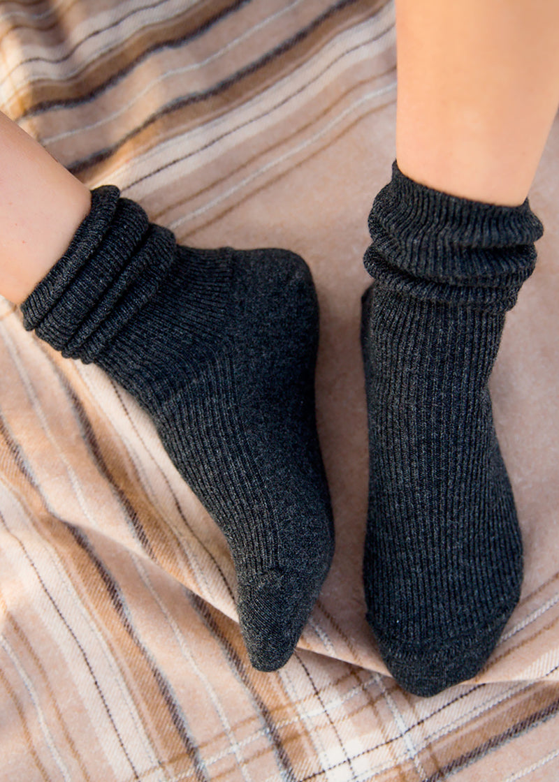 A close-up of a person's feet wearing dark charcoal gray ribbed ankle socks, resting on a beige and brown striped blanket.