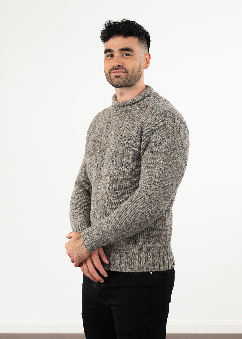 A man wearing a textured gray knit sweater and black pants, standing against a plain white studio background.
