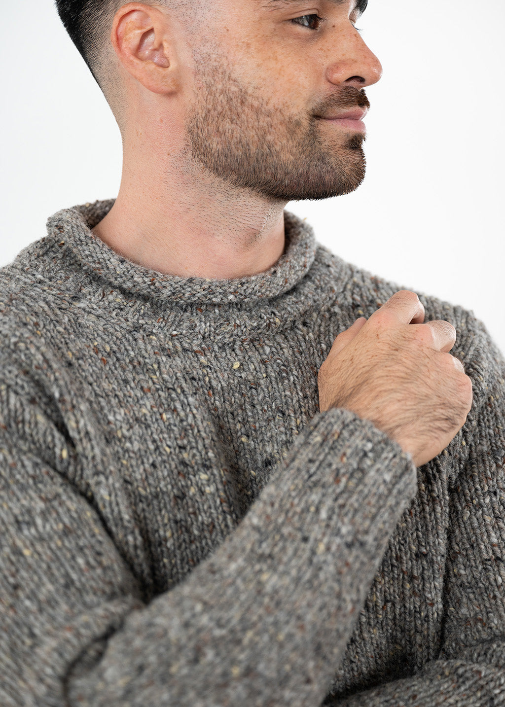 A close-up side profile of a man wearing a textured grey donegal knit jumper with flecks, set against a plain white background.