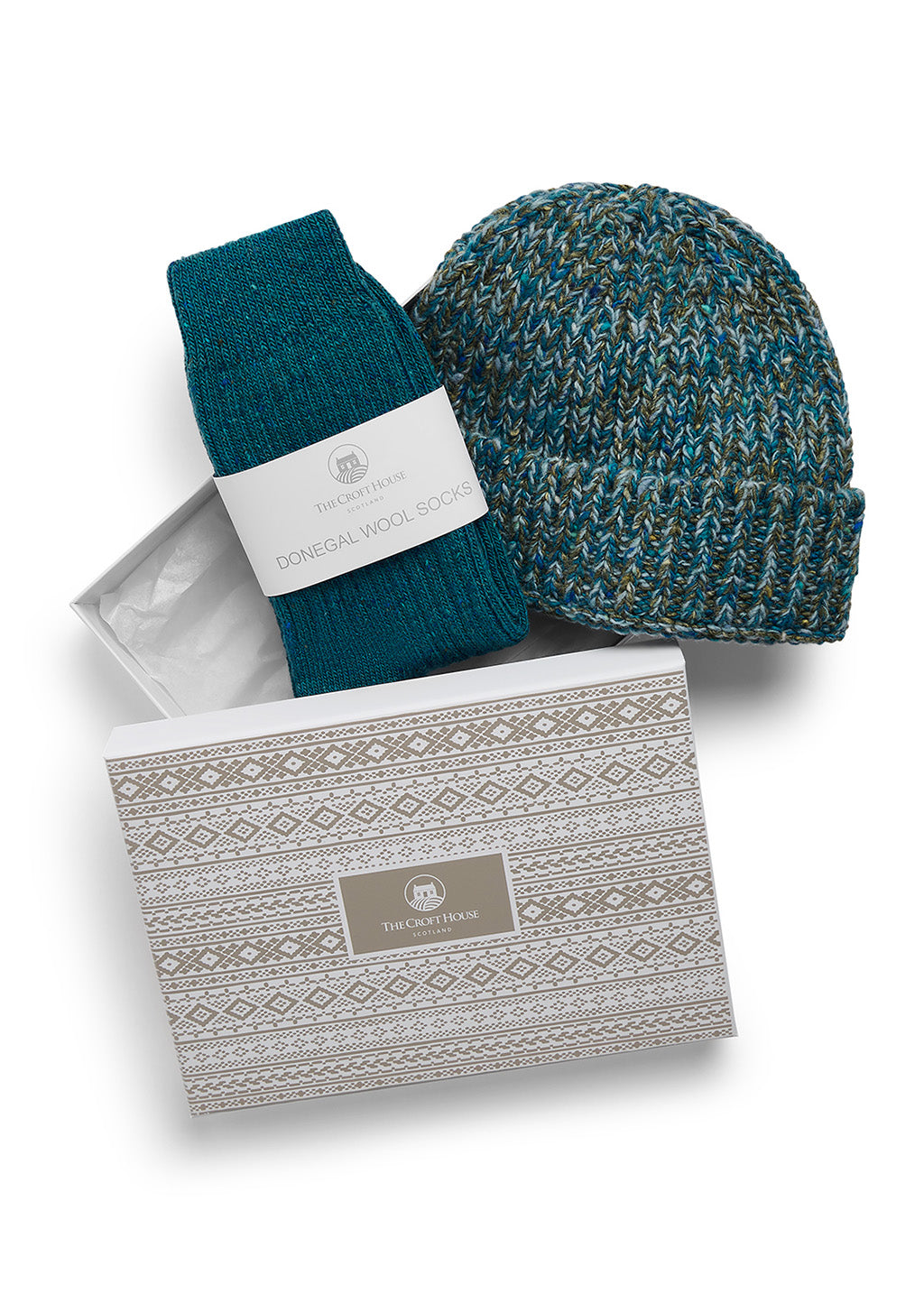 A pair of folded teal wool socks and co-ordinating marled wool beanie hat lying on top of a gift box with beige fair isle patterns and The Croft House logo on the lid, against a white background.