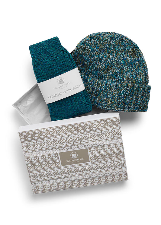 A pair of folded teal wool socks and co-ordinating marled wool beanie hat lying on top of a gift box with beige fair isle patterns and The Croft House logo on the lid, against a white background.