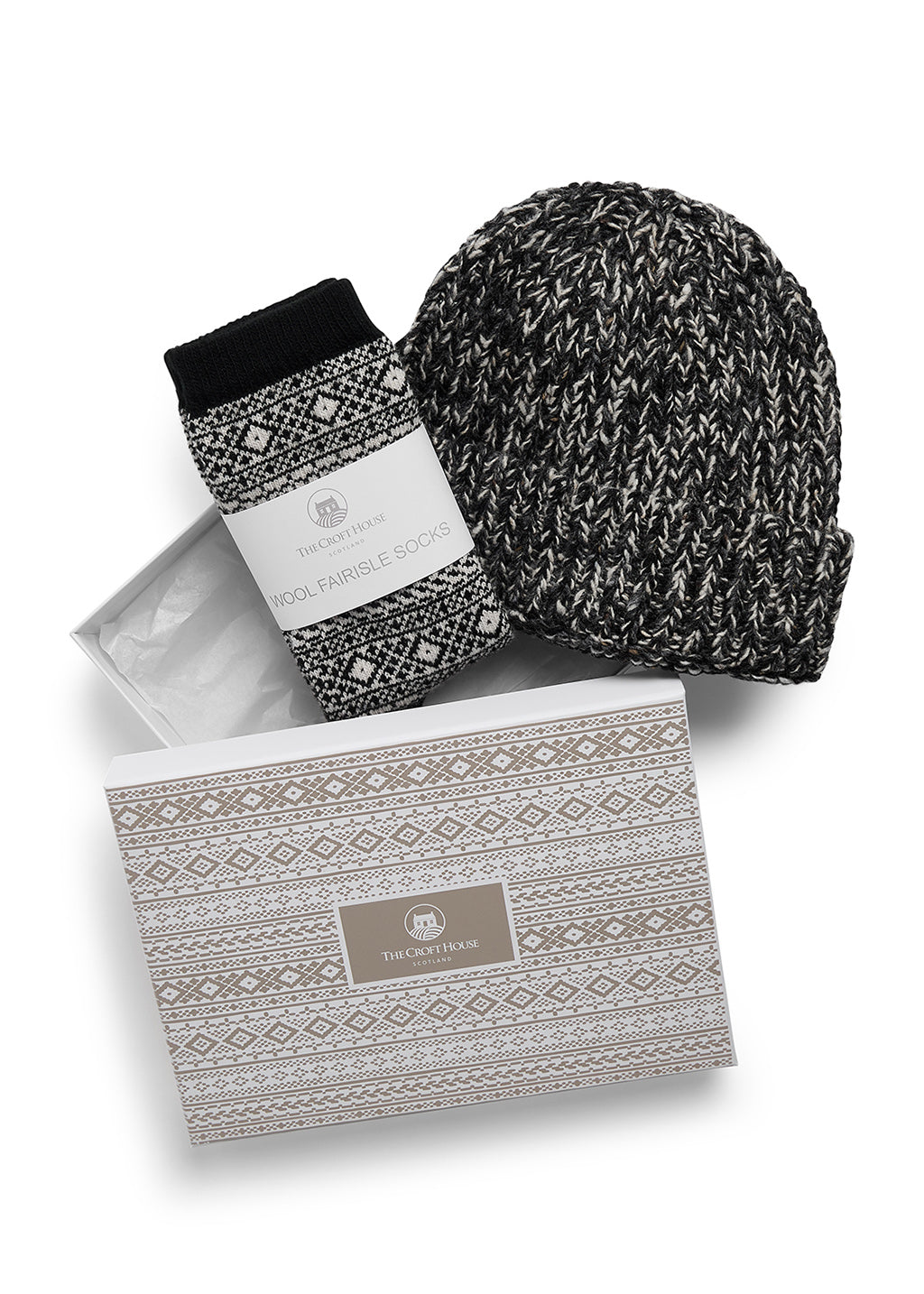 A pair of folded black and beige fair isle wool socks and co-ordinating marled wool beanie hat lying on top of a gift box with beige fair isle patterns and The Croft House logo on the lid, against a white background.