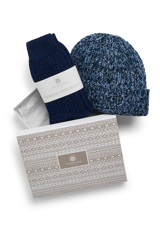A gift set from The Croft House featuring a navy blue marl chunky knit beanie, a navy blue pair of socks with a white paper band, and a patterned gift box on a white background.