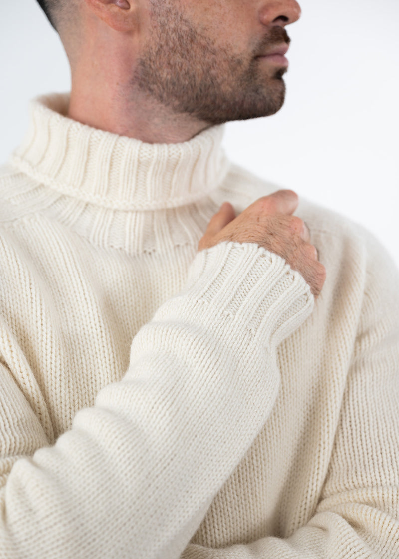 Close-up of a man wearing an undyed wool cream ecru polo neck jumper, showing the texture of the knit and the ribbed collar and cuff.