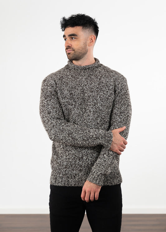A man wearing a long-sleeve marled knit jumper in black and ecru, paired with black jeans, standing against a plain white studio background.