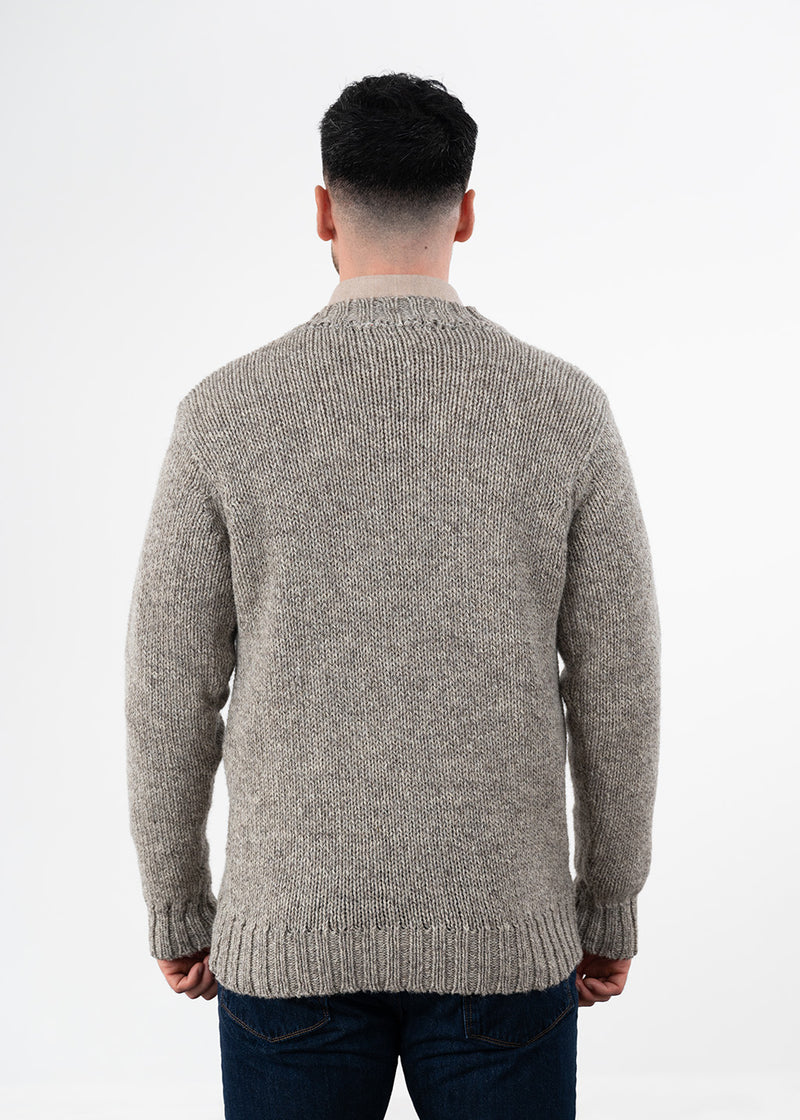 A man viewed from the back wearing a knitted jumper in a heathered taupe-grey colour, paired with dark blue jeans against a plain white studio background.