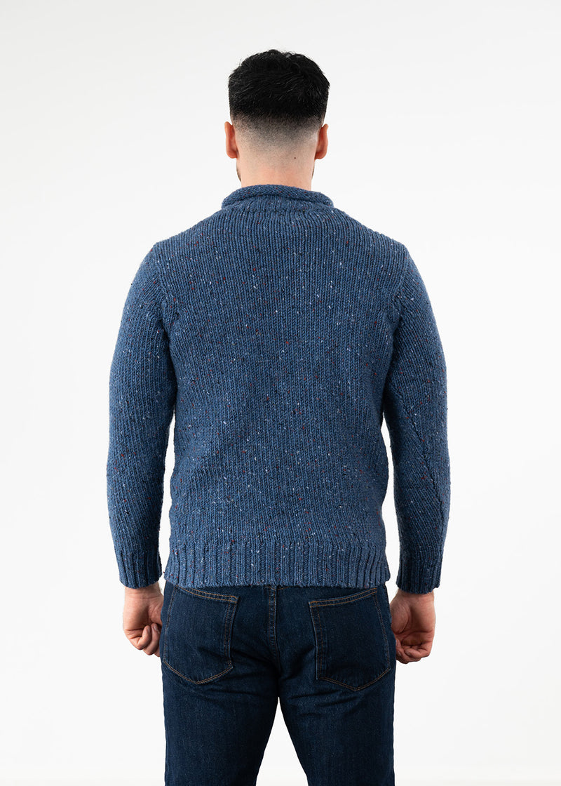 A man viewed from behind wearing a textured blue knit sweater and dark blue jeans against a plain white studio background.
