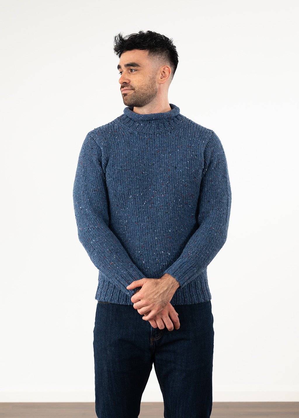 A man wearing a textured blue wool jumper and dark jeans, standing against a plain white studio background.