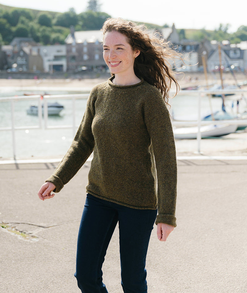 Woman wearing a green wool sweater standing outdoors with a harbour in the background