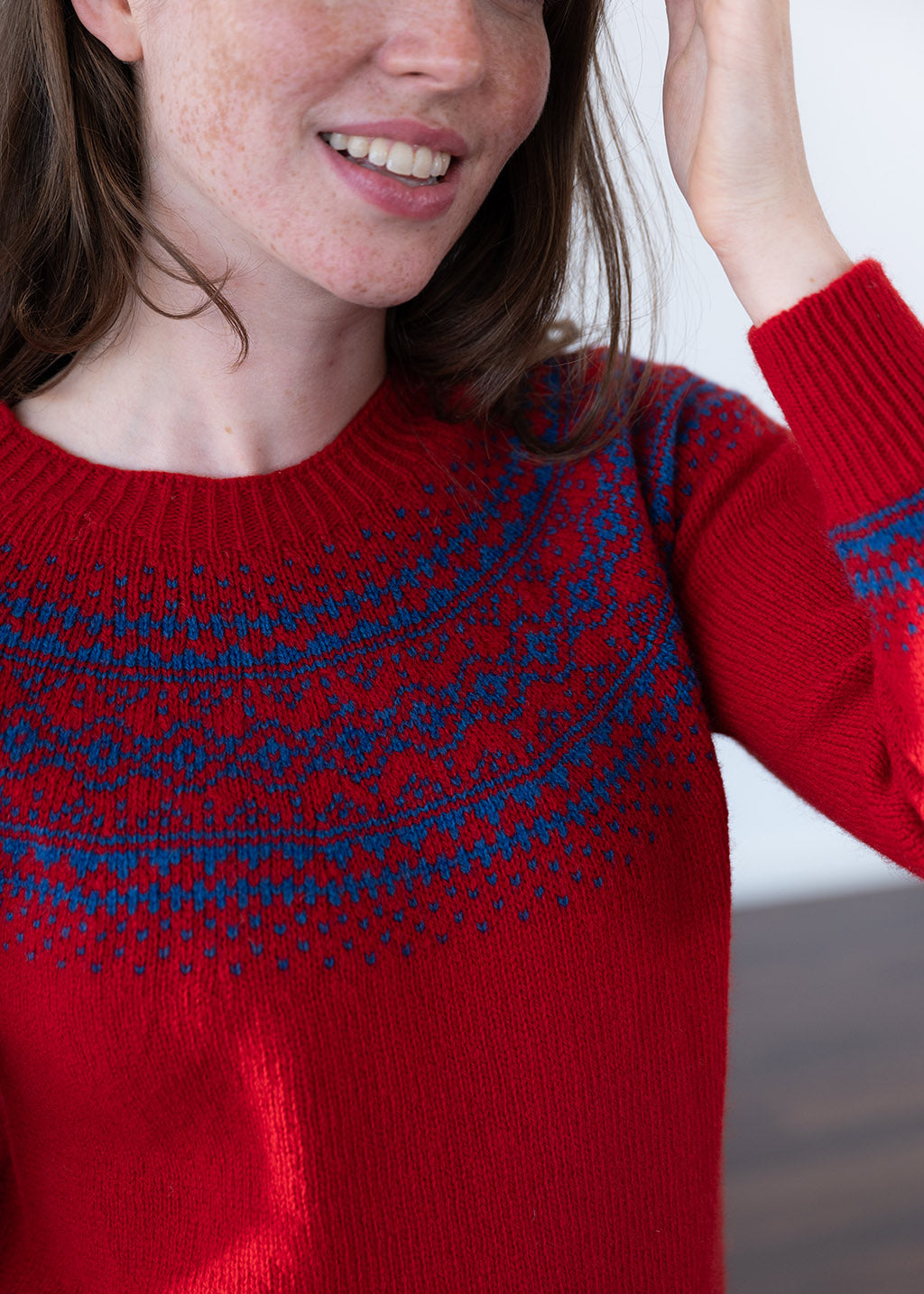 A close-up of a woman wearing a red knit sweater with a blue Fair Isle pattern across the chest, shoulders and cuff.