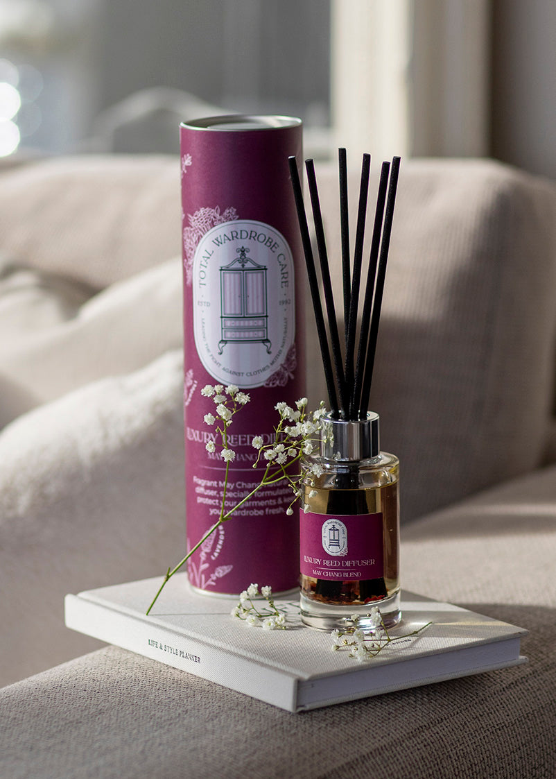 Reed diffuser set with burgundy packaging resting on the arm of a beige settee