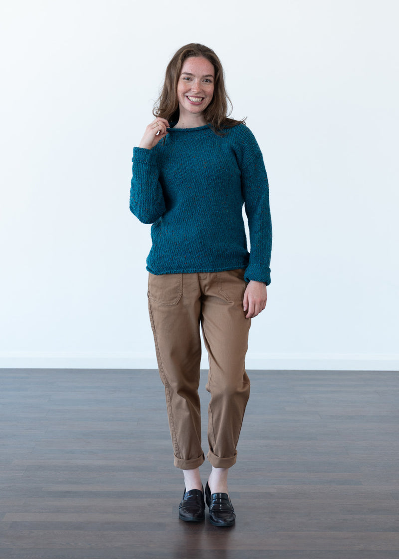 A woman modeling a teal blue textured knit jumper and tan cropped trousers against a clean white studio background.