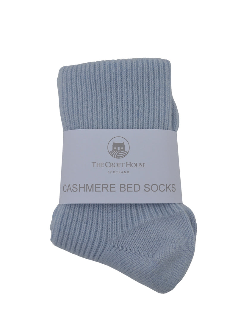 A pair of light blue ribbed cashmere bed socks folded together with a white paper label band that reads 'THE CROFT HOUSE SCOTLAND' and 'CASHMERE BED SOCKS'.