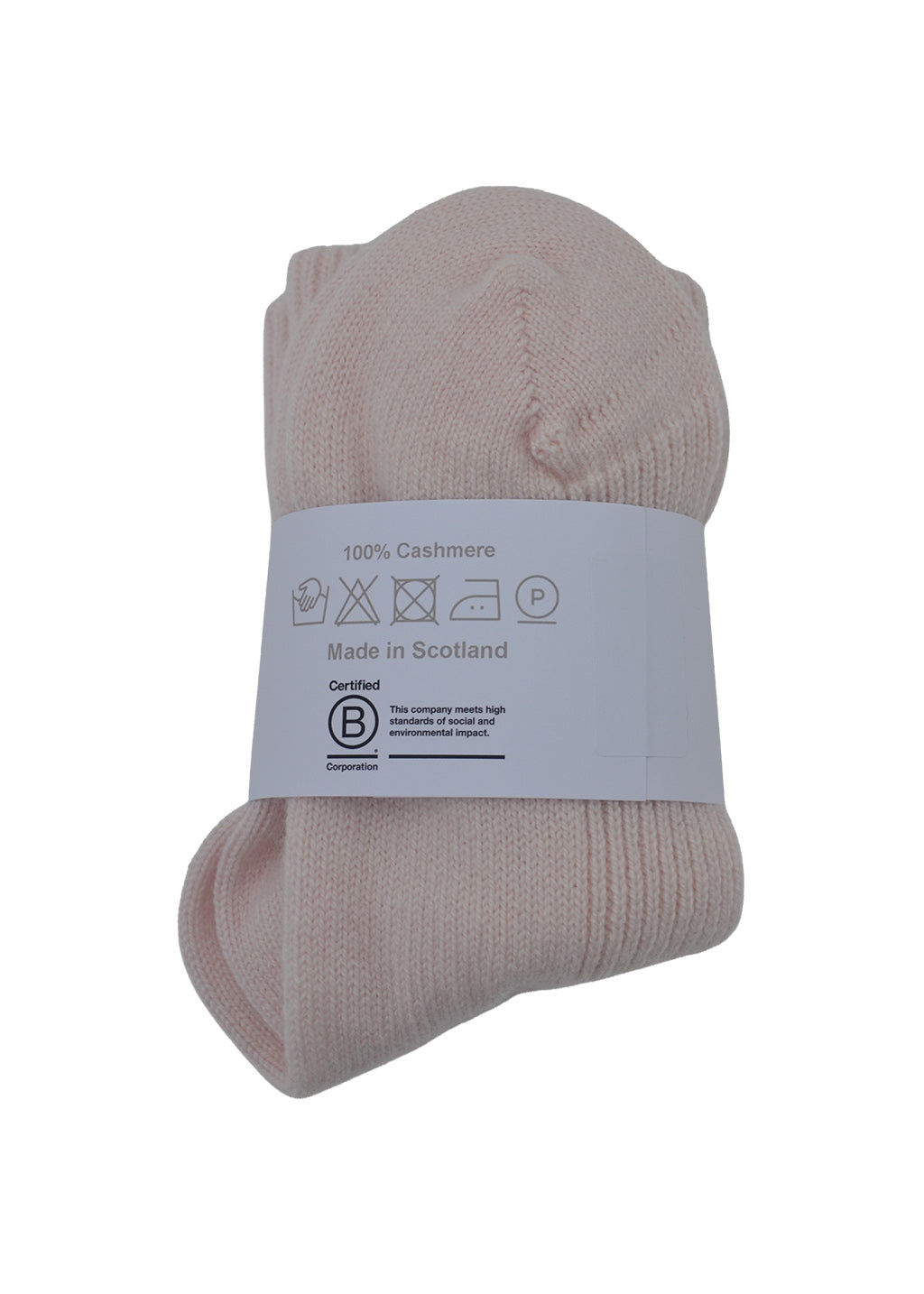 A pair of folded light pink cashmere bed socks with a white packaging band showing washing instructions and the B Corp logo, on a white background