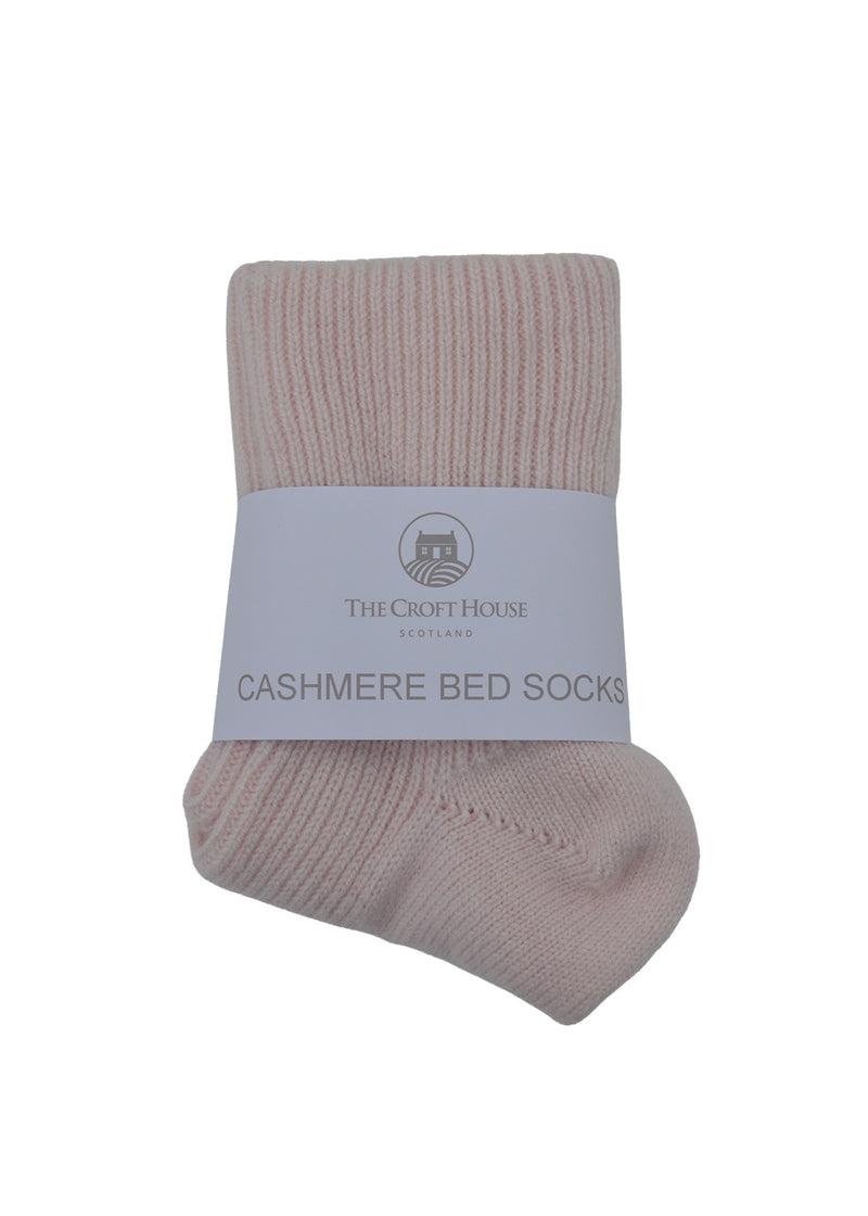 A pair of folded light pink cashmere  bed socks with white packaging band on a white background