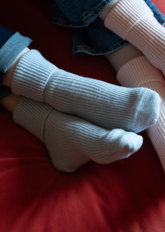 A close up of womens feet wearing pale blue cashmere bed socks whilst lounging on a red settee.