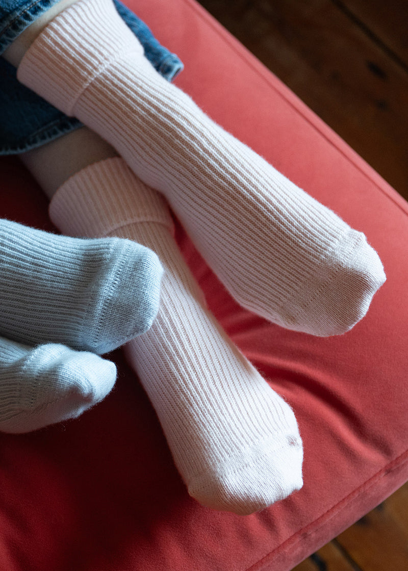 A close up of womens feet wearing pale pink cashmere bed socks whilst lounging on a red settee.