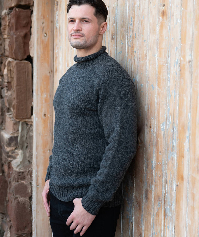 Man wearing a dark grey wool sweater leaning against a wooden door.