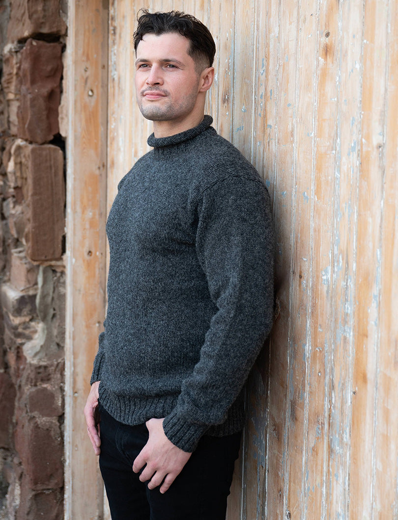 Man wearing a dark grey wool sweater leaning against a wooden door.