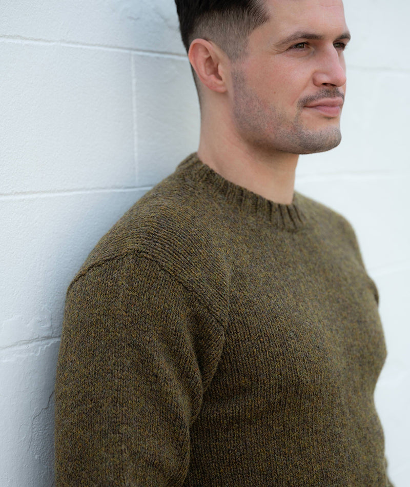 Man wearing a moss olive green sweater against a white wall
