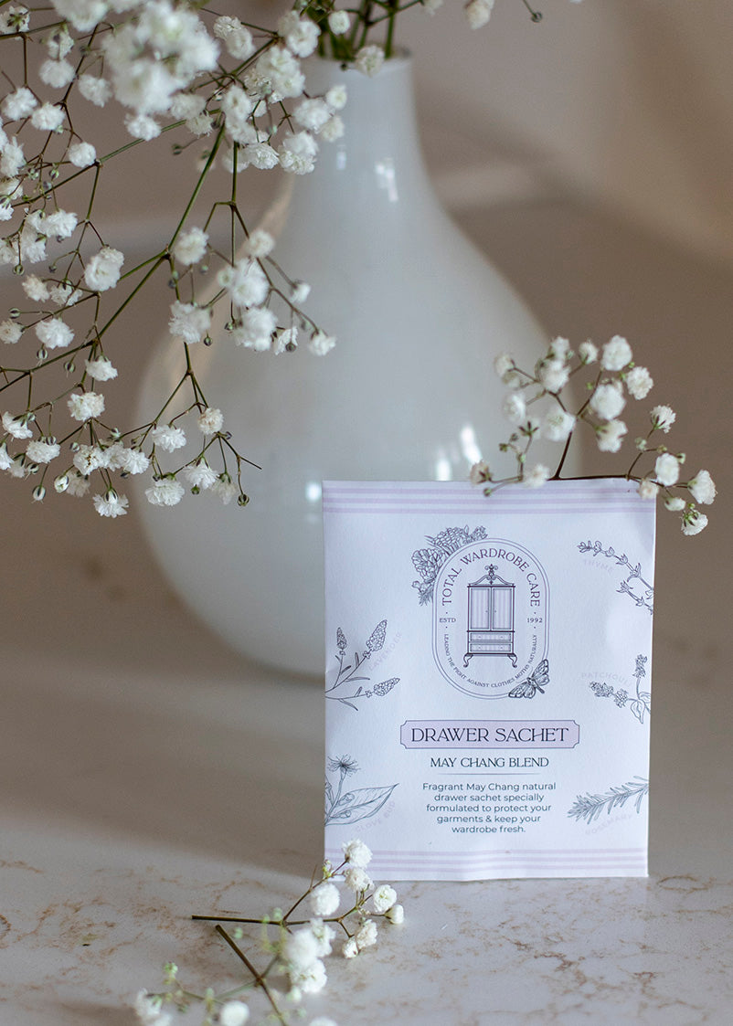 White vase with white flowers and a moth repellent drawer sachet on a marble surface