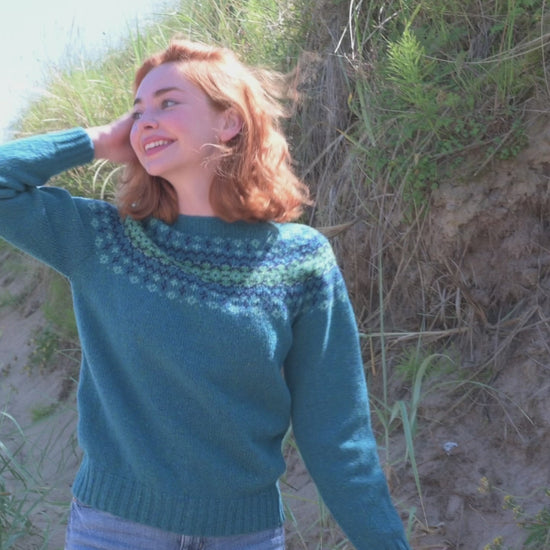A video showing a teal fair isle yoke jumper being modelled amongst sand dunes