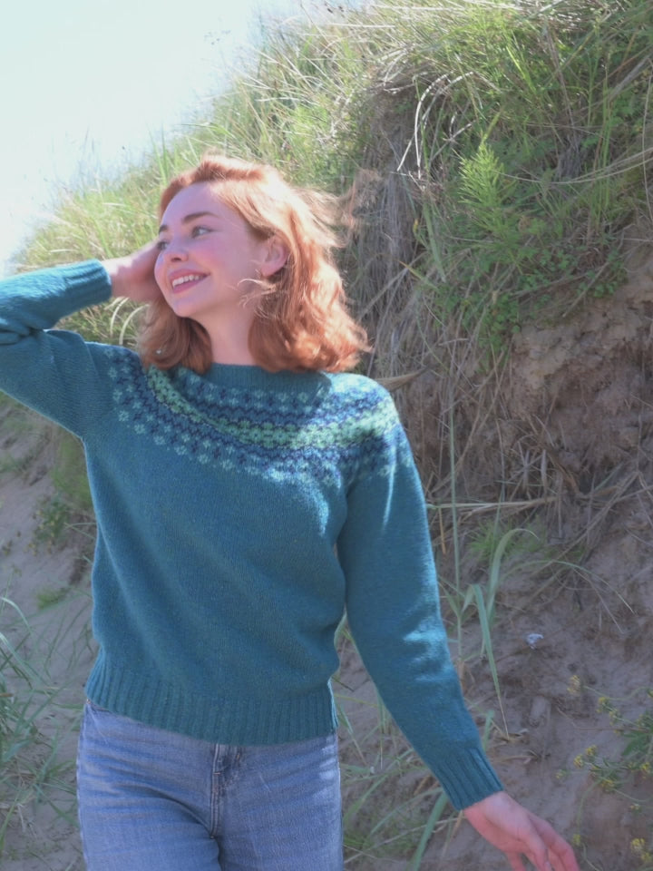A video showing a teal fair isle yoke jumper being modelled amongst sand dunes