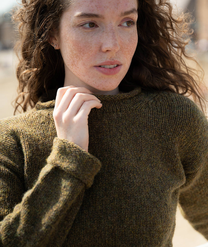 women wearing an olive green jumper with turned back cuffs, holding the rolled neck