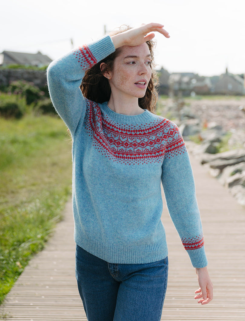 Woman wearing a duck egg blue sweater with red fair isle patterns on a wooden path.